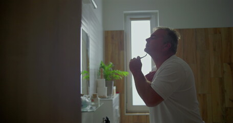 Man preparing for the day, shaving chin and neck area with razor, shaving foam visible, bathroom...