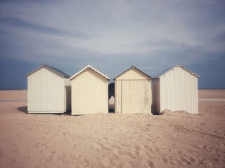 white wooden beach huts on sandy shore under cloudy sky