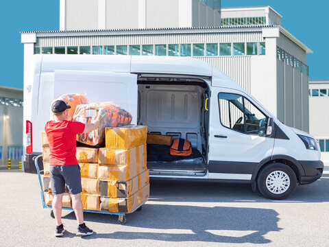 Courier loading packages into delivery van outside industrial warehouse, representing shipping, logistics and express delivery service. &ndash; Delivery, Logistics, Transportation, Courier Service.