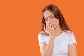 Young woman showing signs of anxiety while touching her face, captured against a bright orange...