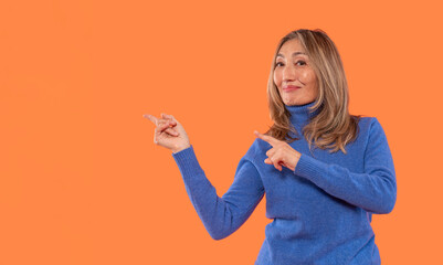 Woman in blue sweater gestures playfully against an orange background during a bright indoor setting