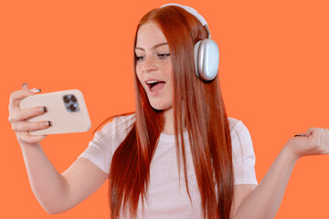 Teen girl reacts enthusiastically while listening to music on her headphones and using her...