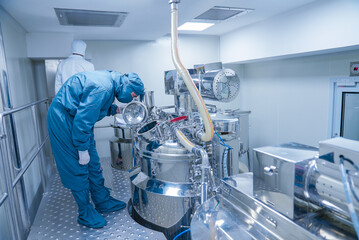 pharmaceutical worker using large machine. person checking medicine liquid making vessel. medicine...