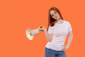 Young woman with red hair holds a megaphone against a vibrant orange background while posing confidently during a promotional event