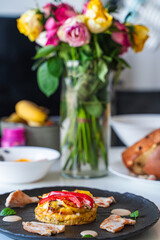 Romantic dinner. Cooked chicken or turkey pieces with potato tartilla and red paprika on a black plate on the table with a bouquet of roses.