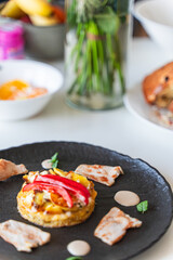 Slices of cooked turkey with potato tortilla and red bell peppers on a black plate with sauce. Beautiful presentation of dinner.
