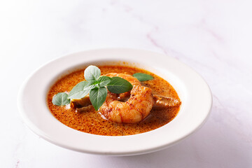 Fresh aromatic hot Thai soup Tom Yum with mushrooms, shrimps and different spices on white marble background close up. Tasty food concept.