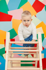 An adorable toddler is energetically climbing up a colorful wooden ladder, surrounded by a vibrant, abstract background that enhances the joyful spirit of childhood exploration and creativity
