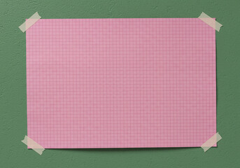 Pink grid paper taped on green wall background.
