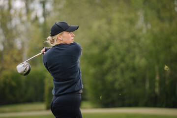 Female golfer completes a powerful swing with a driver, eyes following the ball, grass flying, set on a lush green outdoor course..