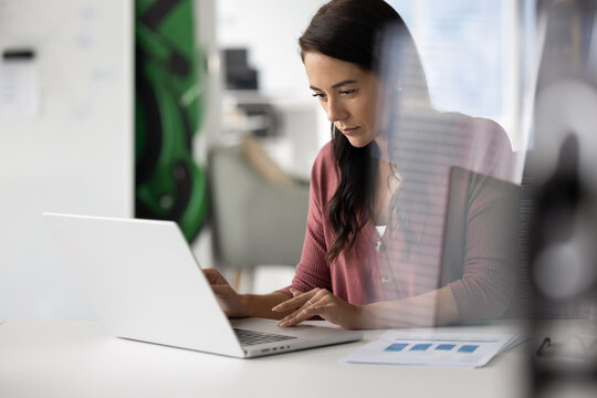 Engaged in data analysis. Portrait busy young woman accountant financial analyst project manager sitting at desk working on statistic report on notebook pc. View through glass office wall. Copy space
