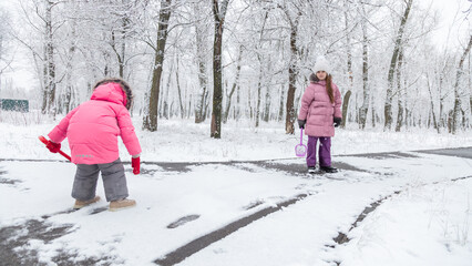 Two little girls in colorful clothes play outdoors during a snowfall.