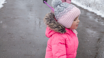Little girl in colorful clothes play outdoors during a snowfall.
