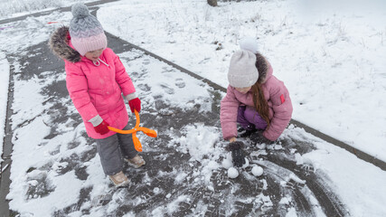 Two little girls in colorful clothes play outdoors during a snowfall.