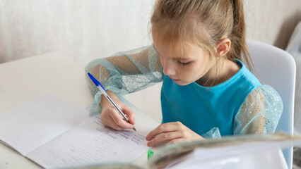 Little school girl sit at table at home write in exercise book prepare homework alone.