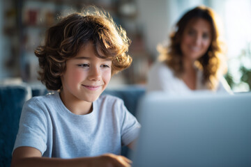 Young smiling boy uses a laptop while his mother watches in the background, representing positive home learning and family support.