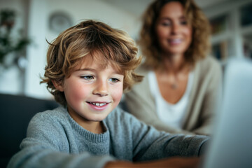 Young boy enthusiastically using a laptop at home while his mother smiles in the background, promoting learning and joy in education.