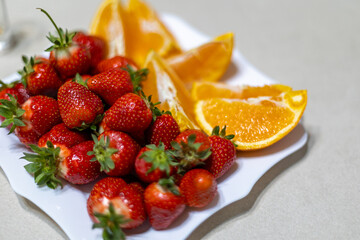 Fresh strawberries and orange slices on plate. Close-up of ripe strawberries and juicy orange wedges arranged on a white plate, perfect for healthy eating and summer recipes.