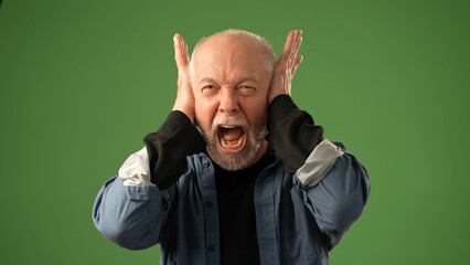 A mature man displays a range of emotions pressing his fingers to his ears on a solid green background. His expression conveys intensity and drama in the moment.