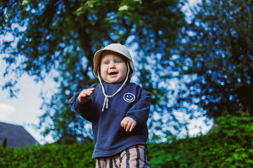 Fototapeta premium A cheerful toddler plays outside in nature, dressed comfortably, smiling brightly under the warm sun, exploring surroundings and seeking adventures filled with pure happiness and laughter