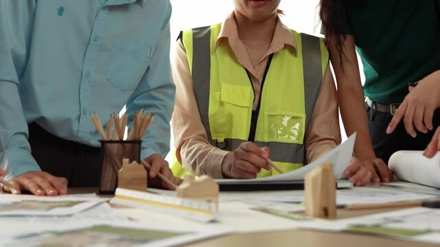 Smart architect and safety engineer discussion about building blueprint on table with architectural document, measurement tools and wooden block scatter around at modern office. Closeup. Delineation.
