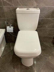 Modern white toilet with closed lid in clean, stylish bathroom with gray marble tiles, Neat interior ideal for homes, hotels, hostels, offices, public restrooms, and healthcare facilities