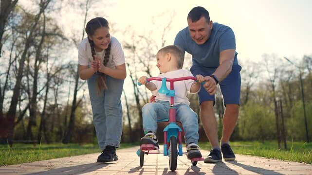 happy family kid. Dad teaches child to ride tricycle in park in summer, showing patience and care. The family enjoys watching the son learning to ride a bike. happy family kid dream concept.