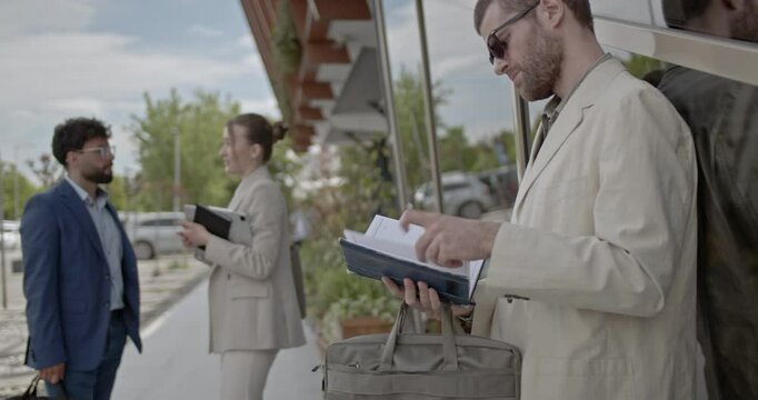 Business people discuss projects in front of an office building. One person checks their phone while two others continue their conversation.