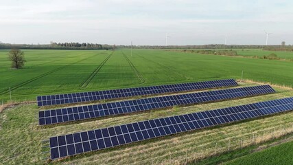 Rows of solar panels on open farmland in Lithuania with distant wind turbines, highlighting clean and sustainable energy use