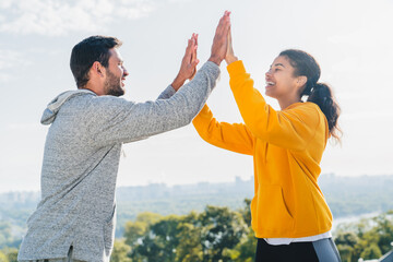 Plakat Sporty couple smiles and high-fives after achieving a milestone during their cardio workout. Strong man and athletic woman giving five on a muscular training. Friends enjoying the wellbeing