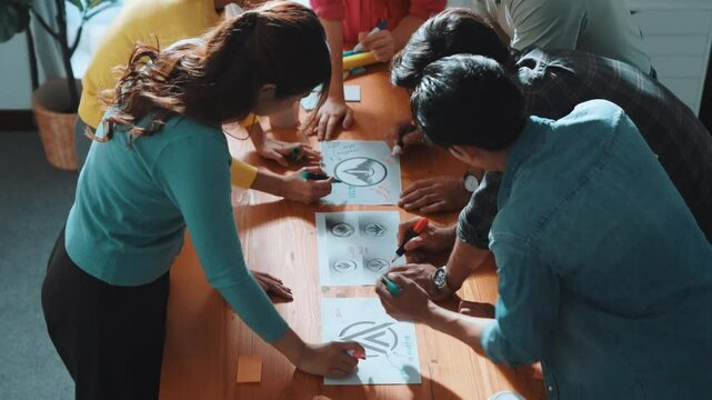 Top view of manager writing idea while team standing and giving comment. Professional designer design logo while looking at color palette and writing idea down in paper with color marker. Symposium.