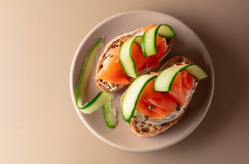 Sandwiches with smoked trout, cream cheese, fresh cucumber and capers on a beige background.