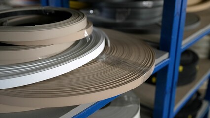 Close-up of plastic edge banding rolls rotating slowly on a metal shelf in a furniture factory, showcasing various colors and materials