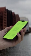 GREEN SCREEN CHROMA KEY Hand holds smartphone by the riverside with historic buildings in the background on an overcast day, ideal for customizable app or branding content