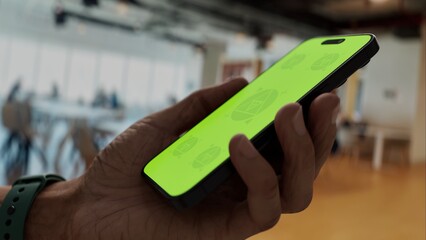 GREEN SCREEN CHROMA KEY Hand holding smartphone with green screen in a modern cafe. Bright indoor setting with casual seating and lively atmosphere