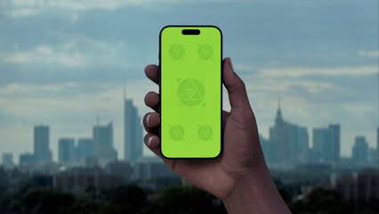 GREEN SCREEN CHROMA KEY Hand holding a phone with a city skyline in the background. Ideal for mockups of taxi, betting, or travel apps set in an urban environment