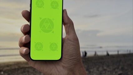 GREEN SCREEN CHROMA KEY Person holding a smartphone at a scenic beach during sunset with silhouettes of people and waves in the background