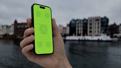 GREEN SCREEN CHROMA KEY Hand holds smartphone by the riverside with historic buildings in the...