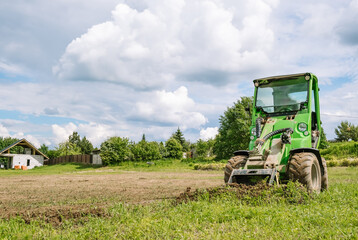 Mini skid steer loader clear a construction site. Small tractor with a ground leveler moves soil. Land work by the territory improvement, plot leveling. Plowing agricultural field. High quality photo.