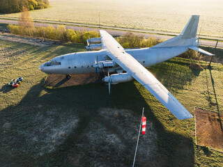 Large propeller transport aircraft on a grassy airfield, top view, illuminated by warm morning or...
