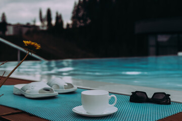 A cozy relaxing pool scene with a cup of coffee, sunglasses, and sandals, perfect for leisure. A serene scene at a pool. Vacation Mode. Do Not Disturb