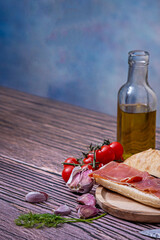 Sliced ​​bread, garlic cloves, seasonings, cherry tomatoes, olive oil, and Serrano ham