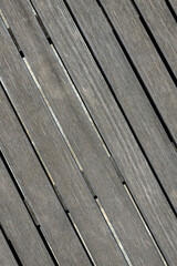 Close-up of aged grey wooden planks laid diagonally with narrow gaps on a concrete base. Visible wood grain texture. Ideal for backgrounds or architectural elements.