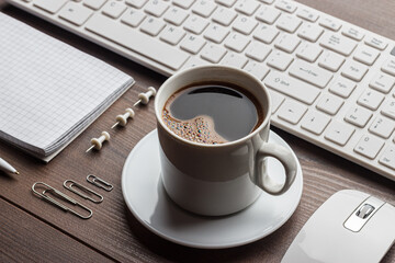 Close-up photo of the office table with notebook, computer keyboard, mouse, cup of coffee.
