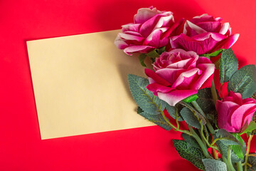 Beautiful pink roses with a blank card on a red surface.
