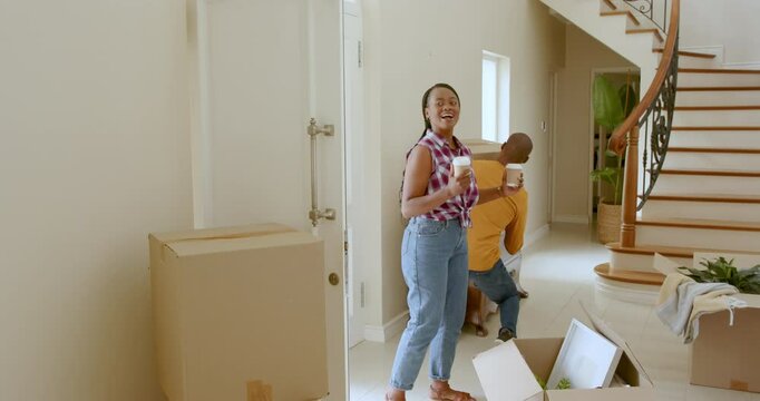 Happy black woman and man embracing holding take away drinks by cardboard boxes, moving into new hom