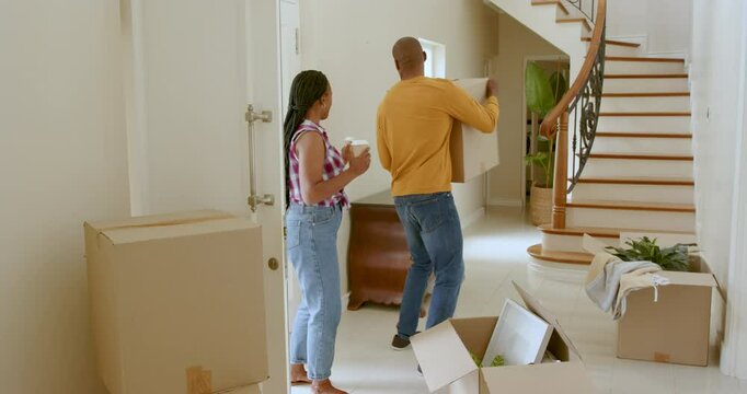 Happy black woman and man embracing holding take away drinks by cardboard boxes, moving into new hom