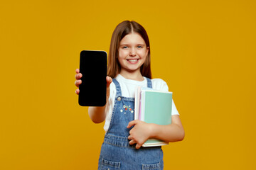 Attractive little kid girl showing smartphone display while holding school books, exuding joy and curiosity. Ideal for educational promotions and tech related advertising.