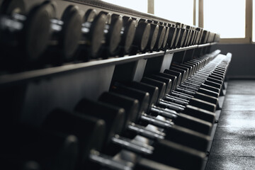 Close up of various weights dumbbells in the row are stored on a sturdy metal rack, ready for strength training or functional fitness workouts.