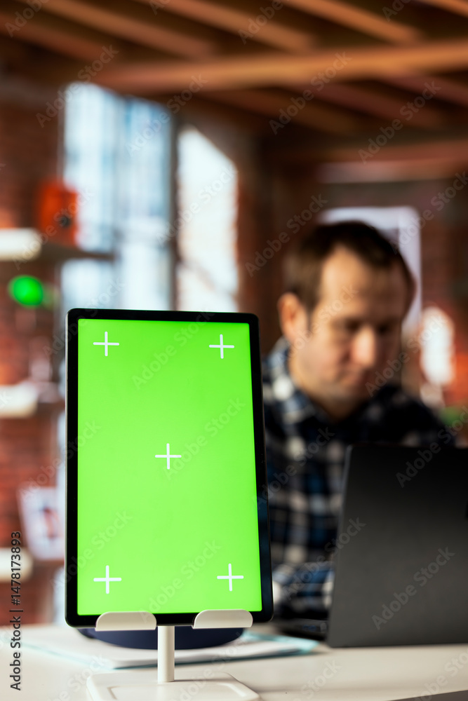 Poster focus on green screen tablet used by employee in blurry background checking emails, reading messages
